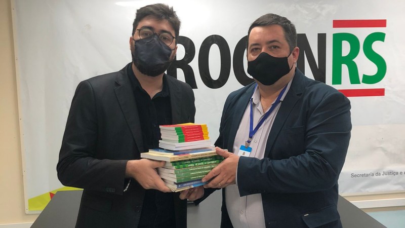 dois homens brancos de cabelos escuros segurando um pilha de livros posam para foto