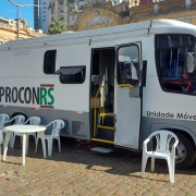 Ônibus branco estacionado com cadeiras na frente. Na lateral do ônibus se lê Procon RS.