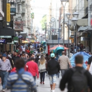 Na foto, há várias pessoas caminhando pela Rua dos Andradas, Centro Histórico de Porto Alegre, e diversos estabelecimentos comerciais.