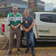 Em frente à caminhonete branca do PROCON RS, estão dois homens brancos, o diretor-executivo do PROCON estadual, Rainer Grigolo, de colete do PROCON, e ao lado dele está o coordenador do Procon de Santo Ângelo, Walter Portalete, de camisa azul. 